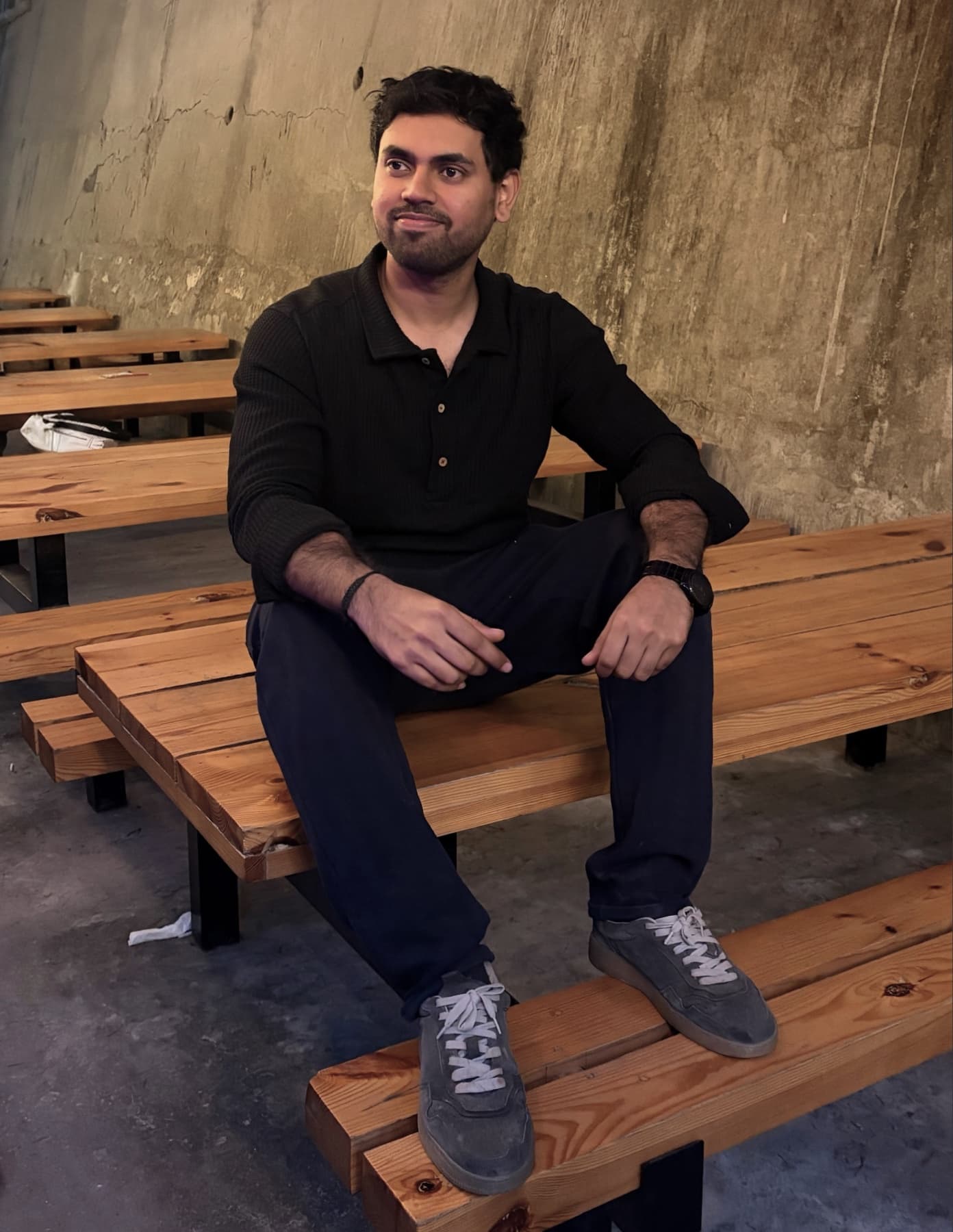 Nitish sitting on a wooden bench against a concrete wall